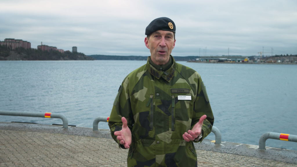 ÖB Micael Bydén i grön uniform på kajkant med vatten i bakgrunden