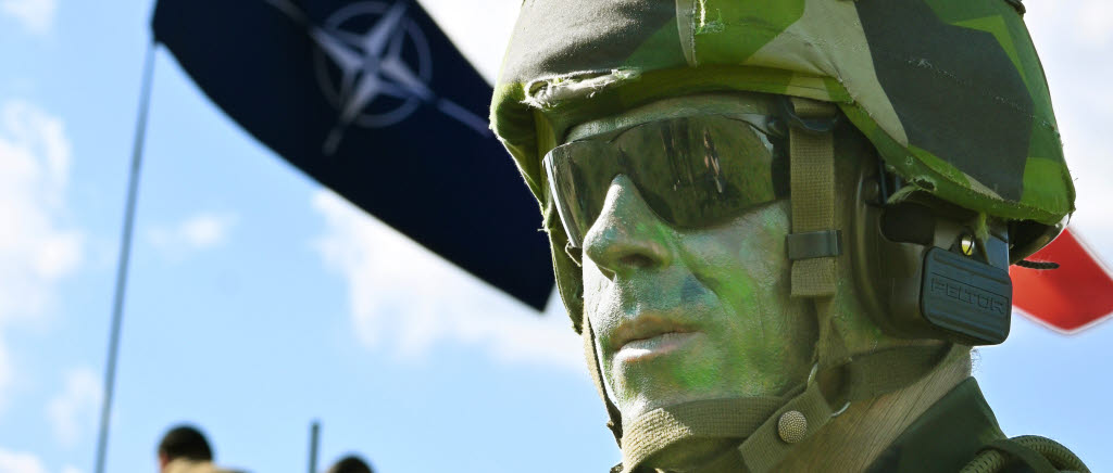 En hemvärnssoldat med stridsutrustning under en övning med en Natoflagga i bakgrunden. 