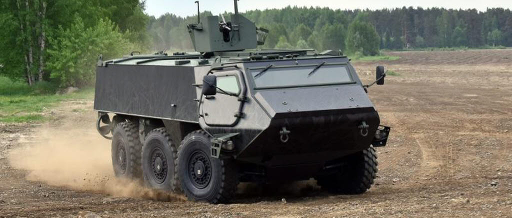 En pansarterrängbil på ett fält. Bilen har 6 hjul. Den kör och svänger. 