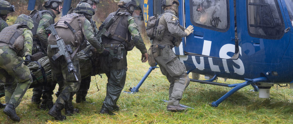 Personer i grön uniform bär en bår och går fram mot en helikopter.