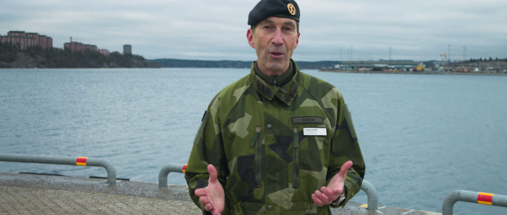 ÖB Micael Bydén i grön uniform på kajkant med vatten i bakgrunden