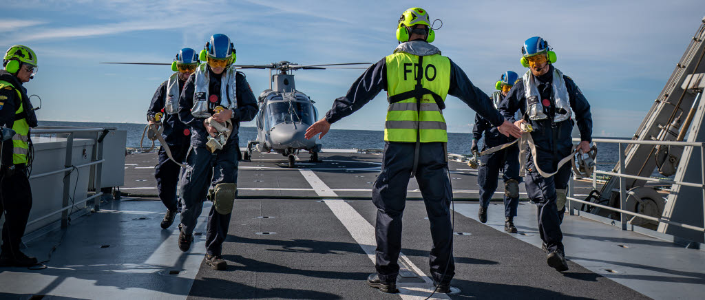 Flight deck officer, FDO är den som leder arbetet på däck och som pratar med flygkoordinatorn på bryggan. Piloterna håller han kontakt med genom tydliga handsignaler. Till sin hjälp har FDO:n en flight deck assistant, FDA som är insatsledare och beredd att arbetsleda säkerhetsarbetet på däck i samband med start och landningar. Skulle något hända leder FDA räddningsinsatserna.

Logistikofficer Melker är en av FDO:erna som utbildats och numer har en ny tillikauppgift.

”Eftersom vi varit samlade på samma plattform har vi kunnat prata med piloterna om vad de tycker är bra eller dåligt i hur vi gör. Det har varit väldigt utvecklande, säger Melker.

Militär flygplats till sjöss. För att säkerställa funktionen har marina fartygsbesättningar drillats under en vecka i september ombord på HMS Carlskrona. Det är Marinbasen som har uppdraget att genom HMS Carlskrona se till att helikopterlandningsförmågan till sjöss inom marinen bibehålls och även taktikutvecklas tillsammans med 3:e helikopterskvadronen.