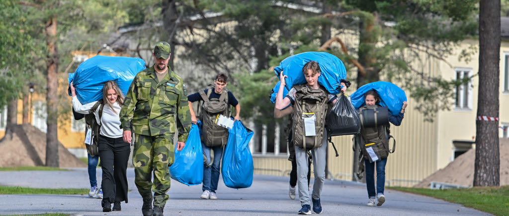 Rekryter i civila kläder bär på stora blå plastpåsar. 
