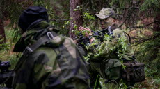 Två grönklädda soldater gestikulerar till varandra i skogen. 