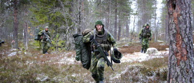 Soldater från Livgardet springer med utrustning i en skog. 