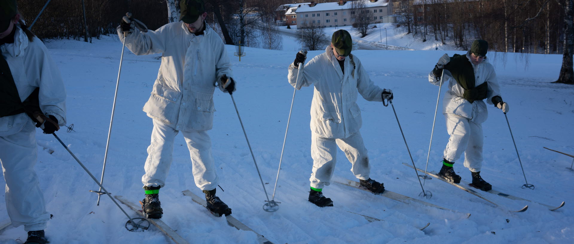 Soldater i vita snökläder  på skidor kliver uppför backe  sidledes