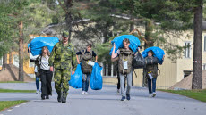 Rekryter i civila kläder bär på stora blå plastpåsar. 