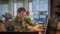 Två män i uniform sitter vid datorskärmar och kartor