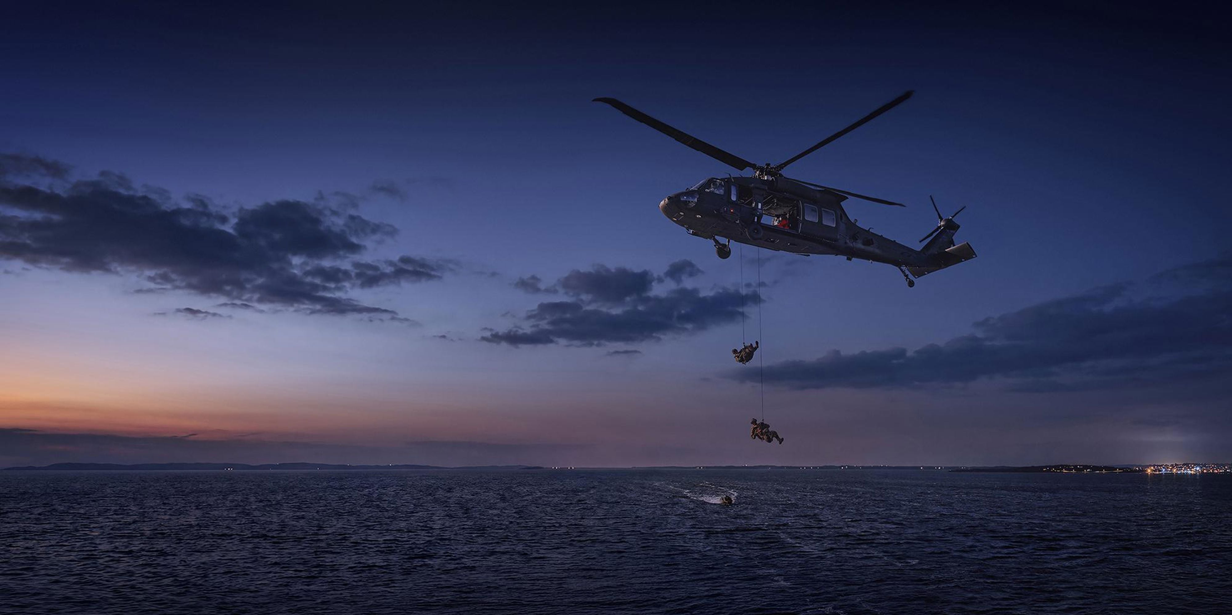Två soldater som hänger med rep från en helikopter över havet.