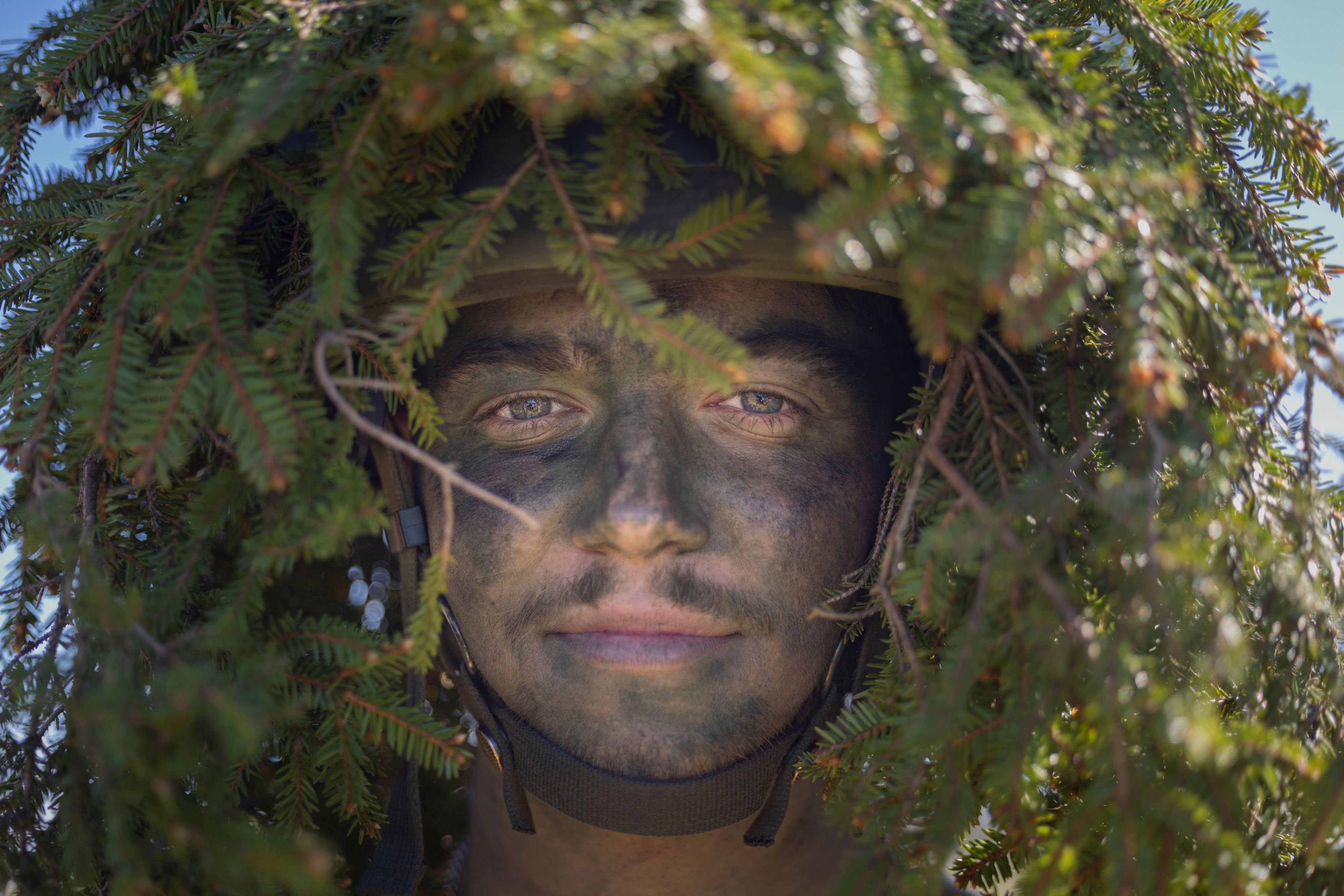 Manlig soldat som är kamouflerad med barr