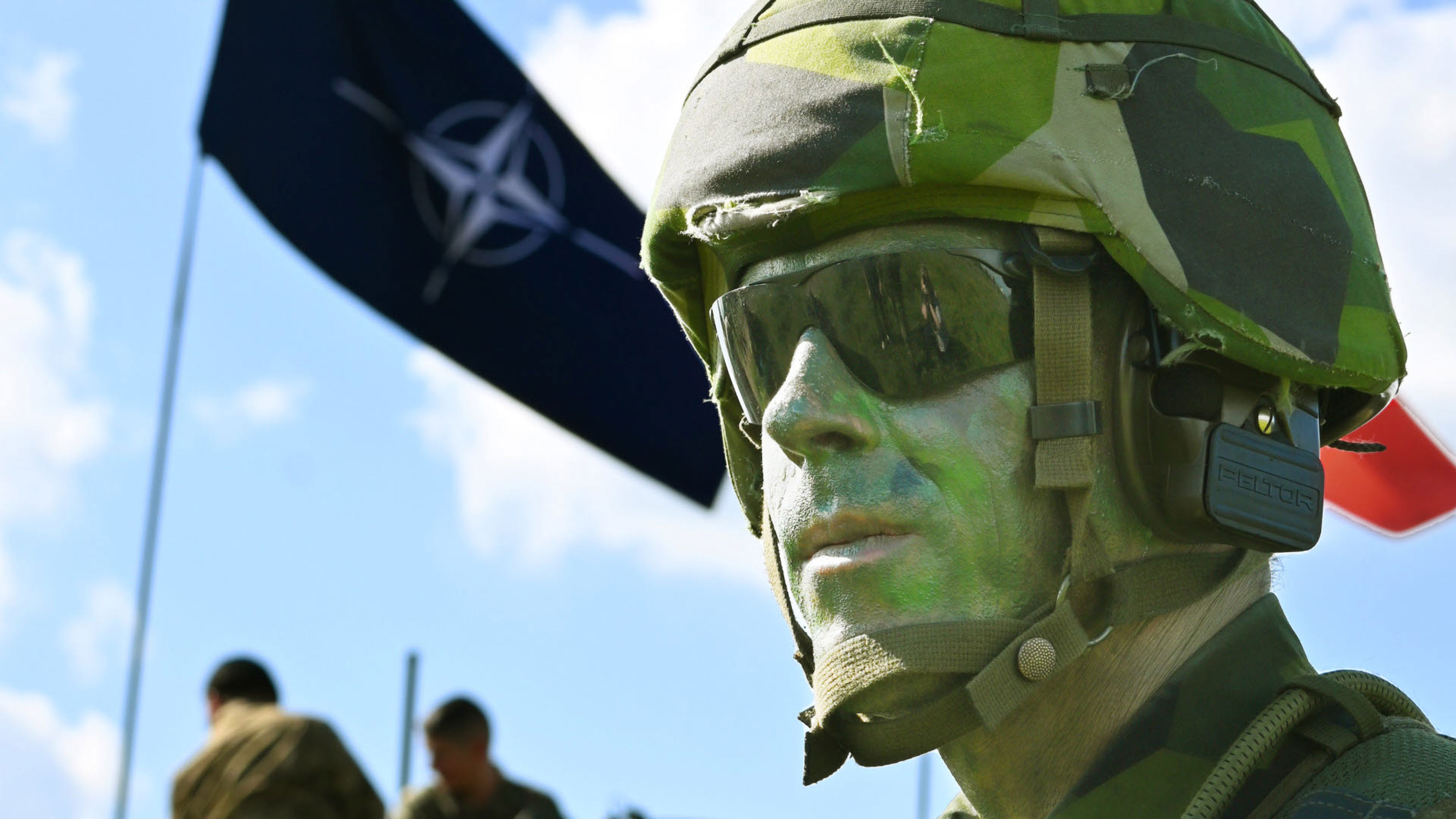 Kamouflagemålad soldat med Natoflagga i bakgrunden