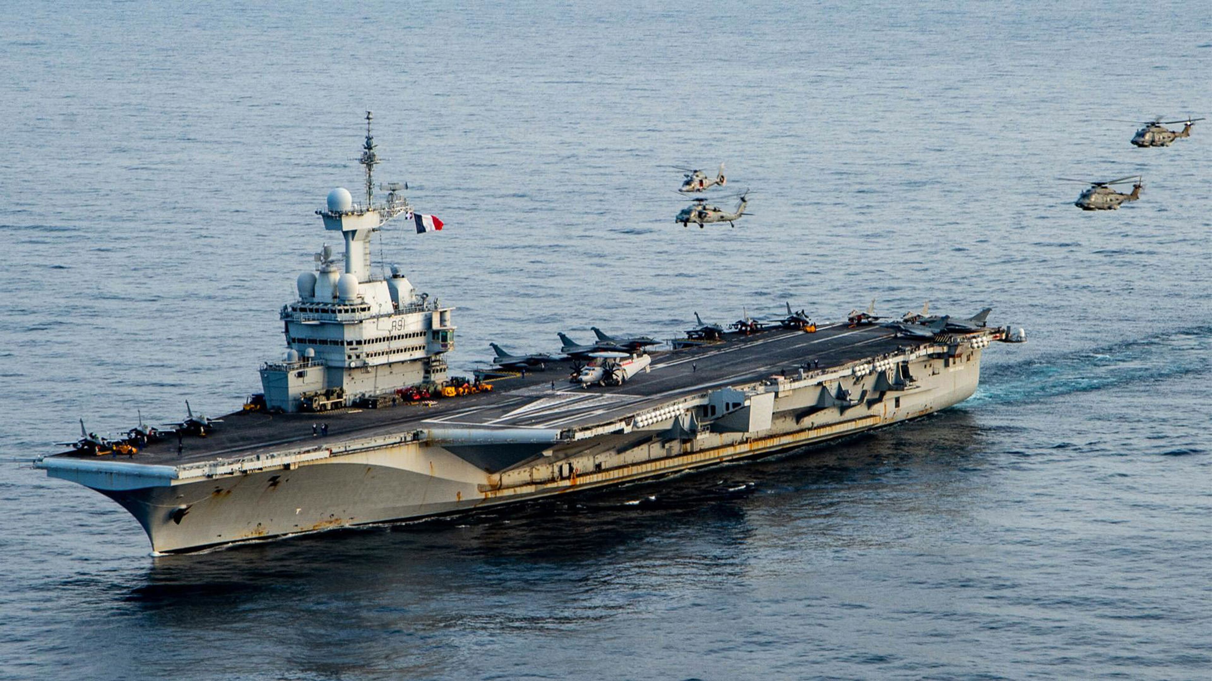 Hangarfartyg ute på havet med helikoptrar flygande bredvid.