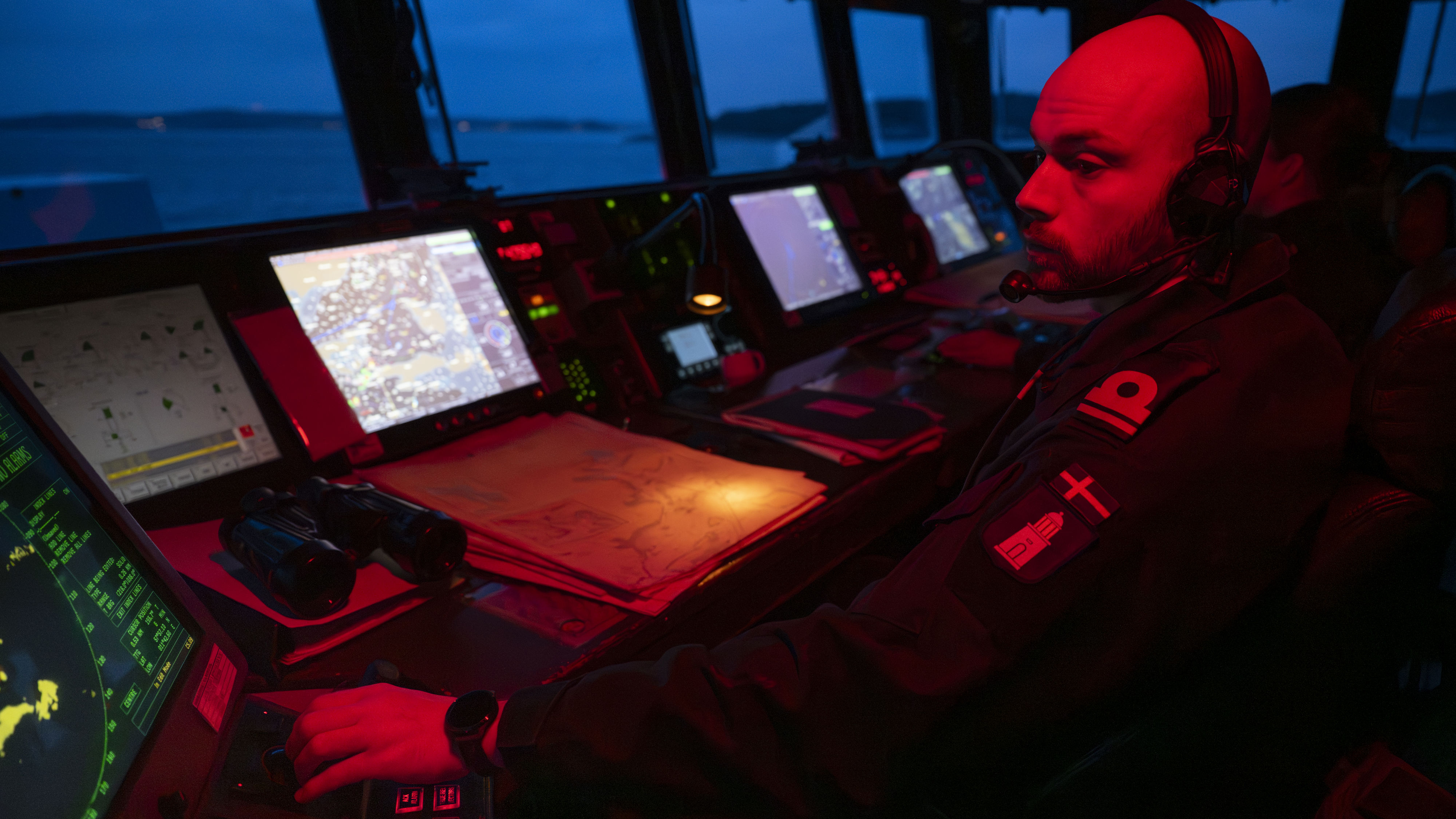 Det är skymning. En sjöofficer sitter på bryggan, endast upplyst av rött ljus. Skärgården är mörkt blå utanför fönstret. Många skärmar och apparater är framför officeren.