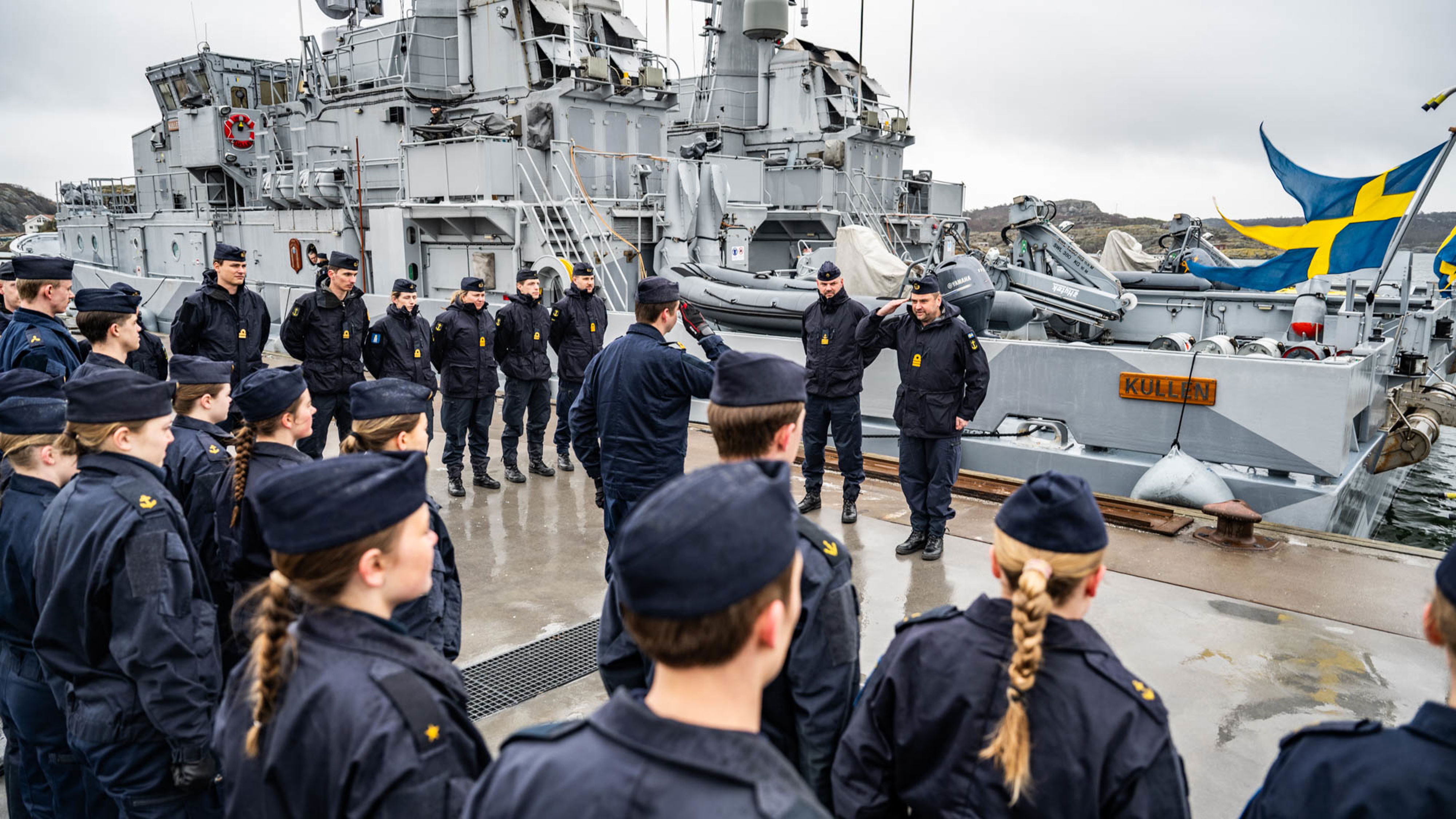 Avlämning med marinens personal på en kaj framför två grå minröjningsfartyg.