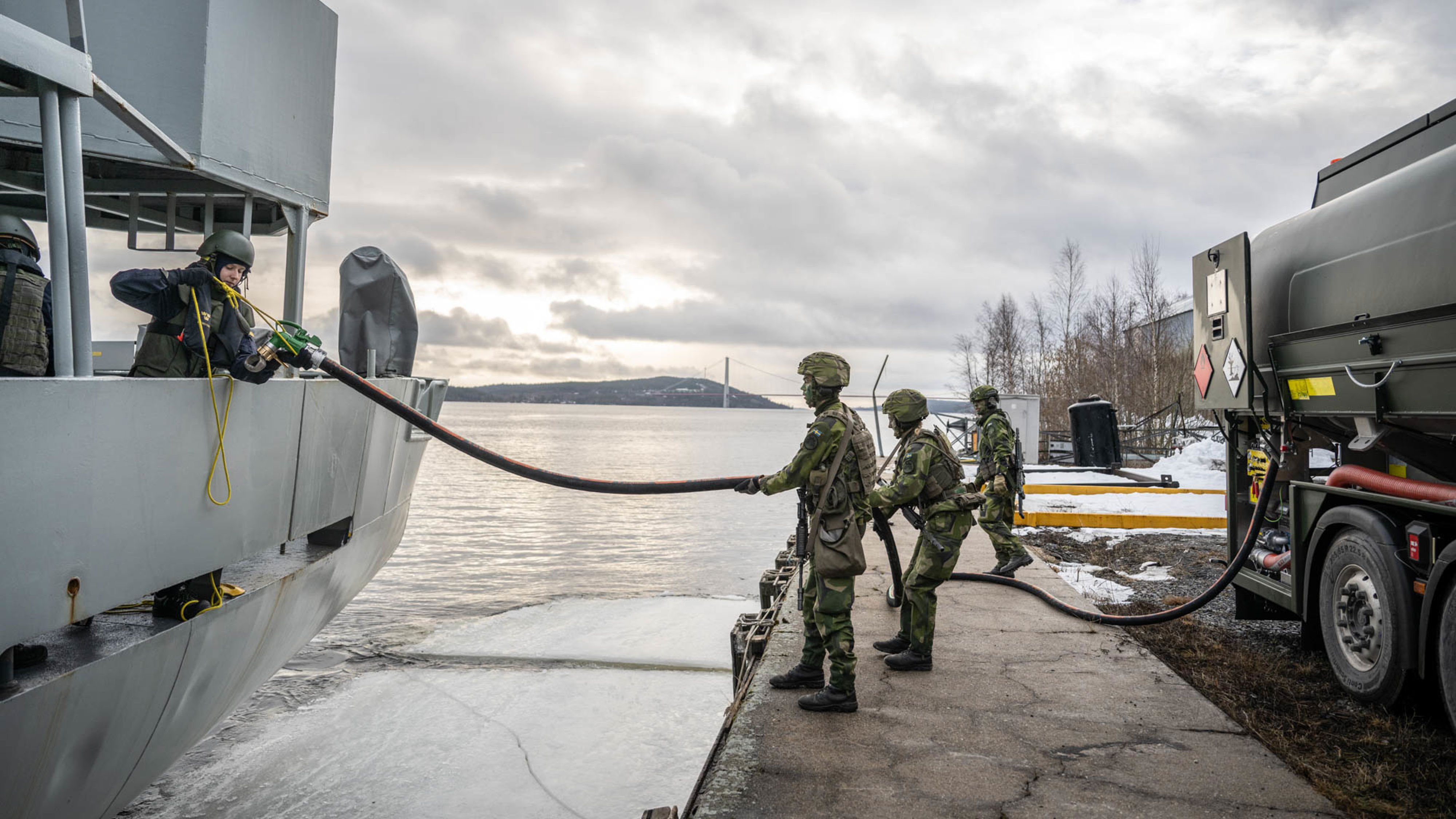 Grönklädda soldater och sjömän tankar ett grått fartyg från en grön tankbil.
