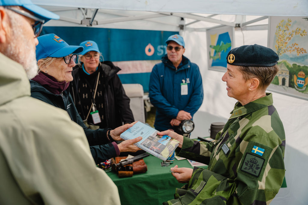 En uniformerad kvinna samtalar med en grupp civilklädda personer i ett vitt tält