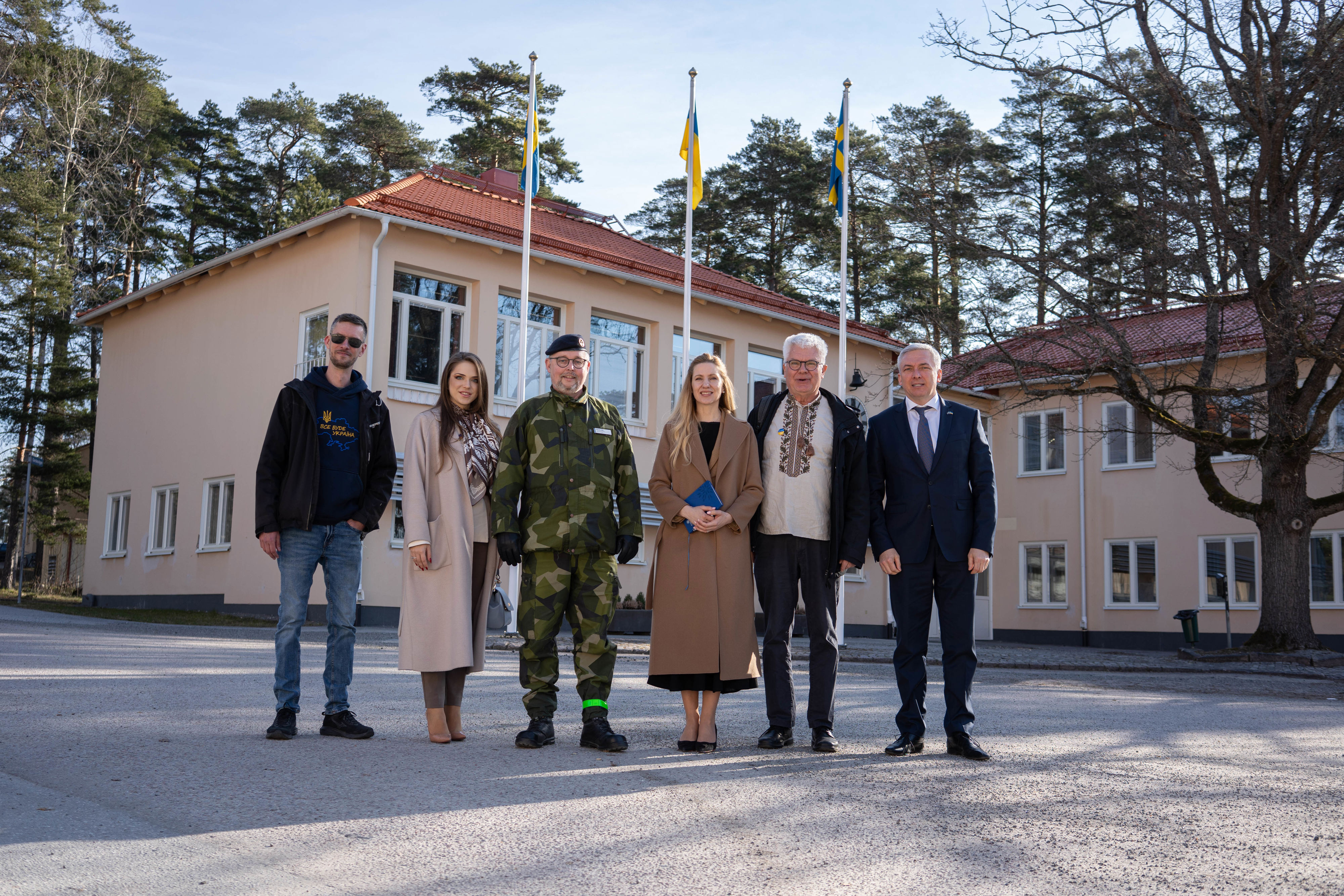 Sex personer står uppställda framför en byggnad med svensk och ukrainsk flagga i bakgrunden.