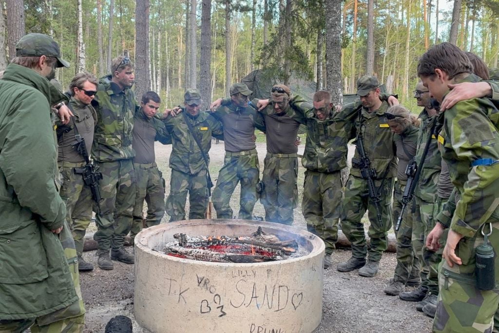 Värnpliktiga håller om varandra runt en eldstad.