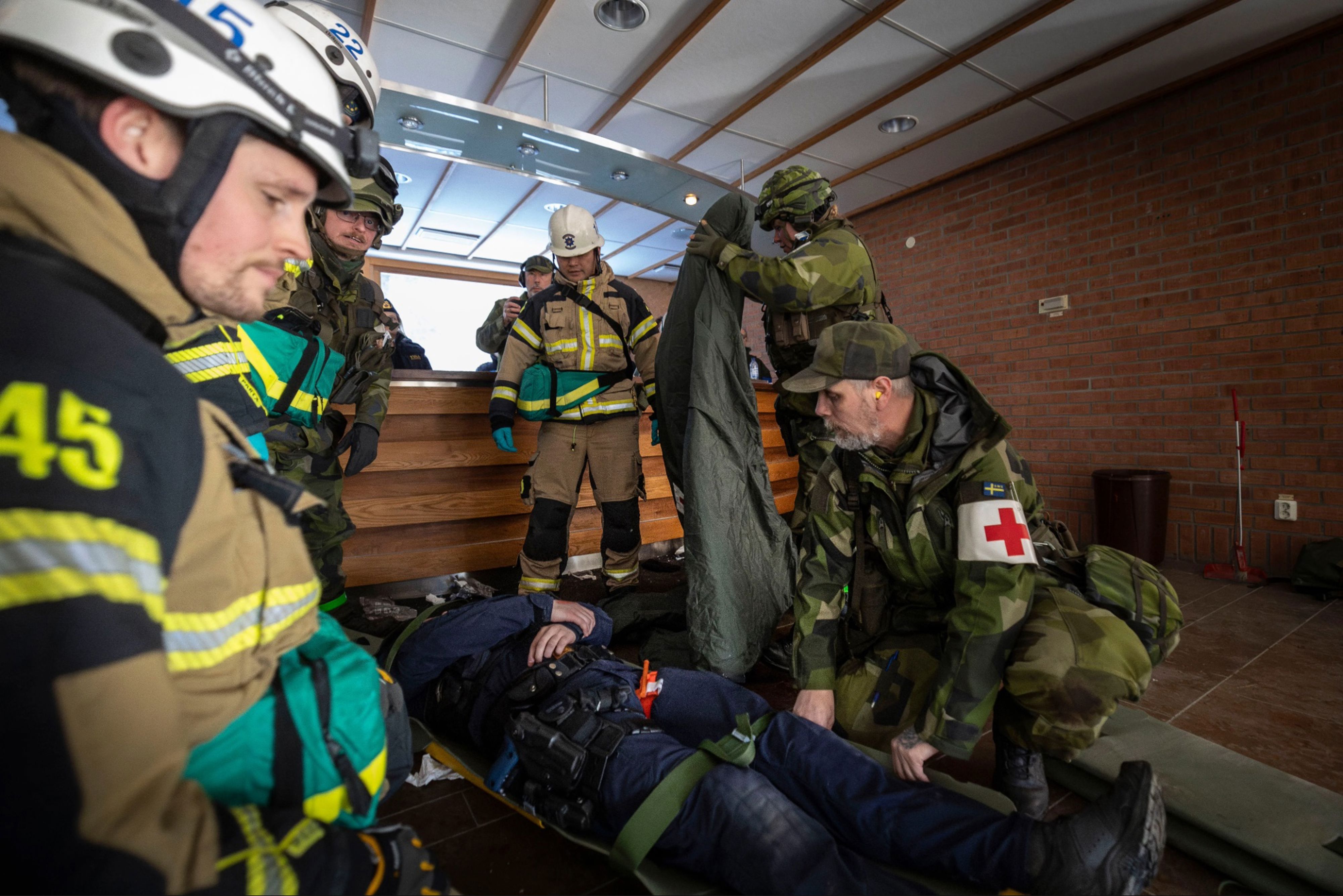 En polis ligger skadad på en bår och sjukvårdspersonal ur hemvärnet och Storstockholms brandförsvar tar hand om mannen.