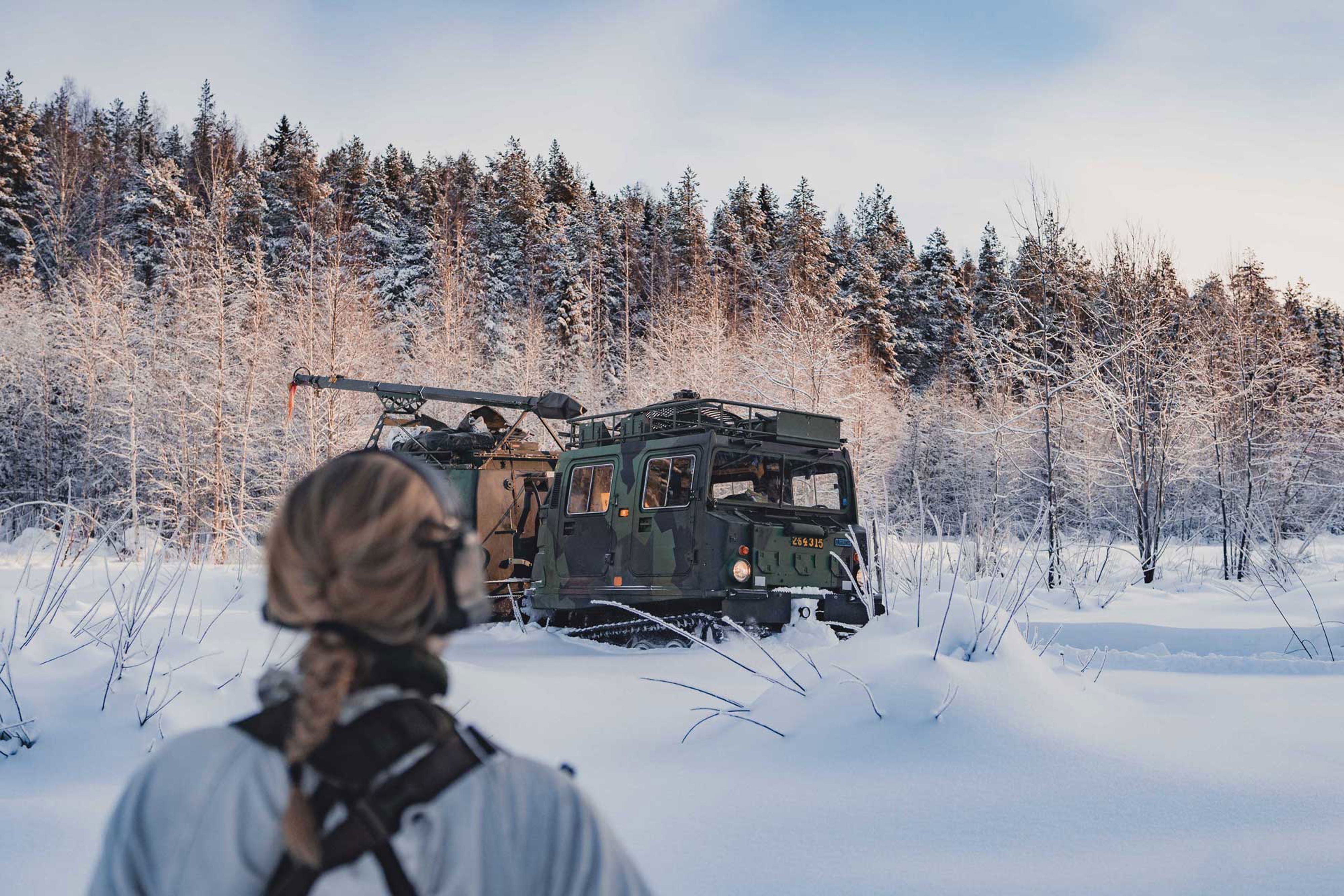 Kvinna som står och tittar på ett stridsfordon i skogen på vintern.
