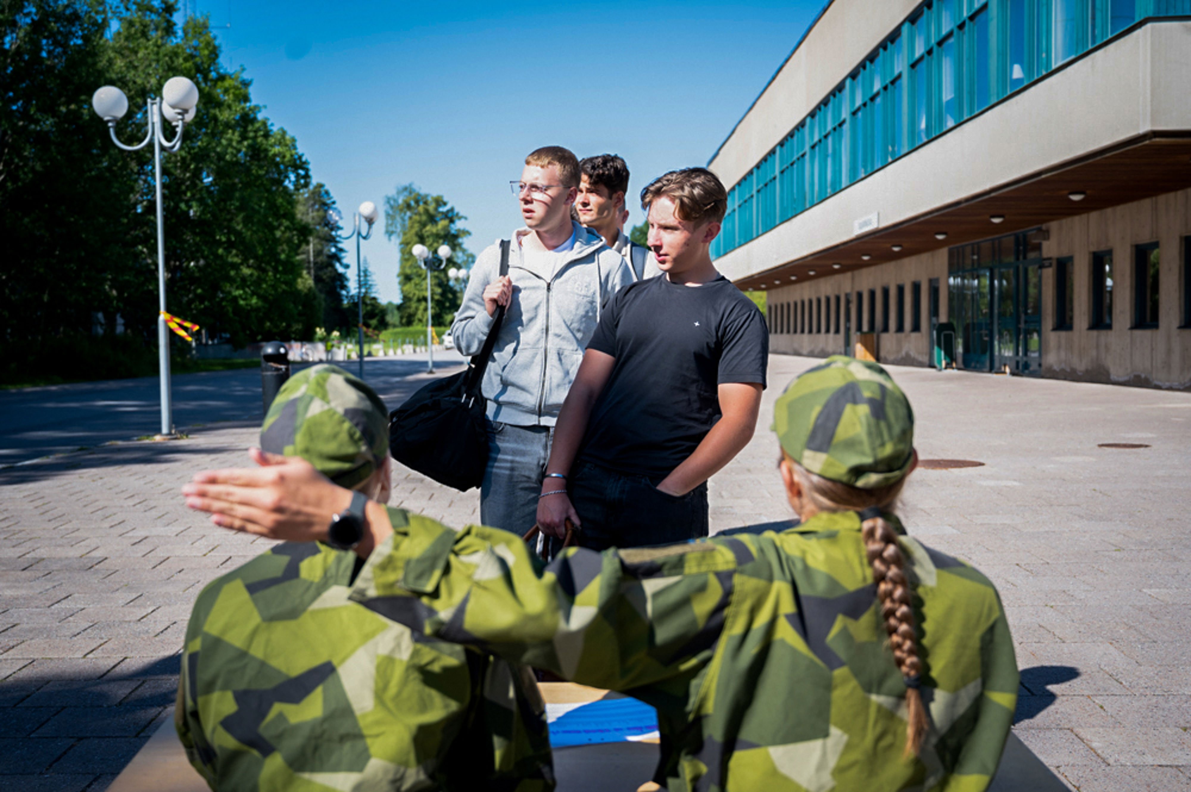 En rad med civilklädda ungdomar står på led framför två sittande soldater som pekar åt vilket håll de ska gå.