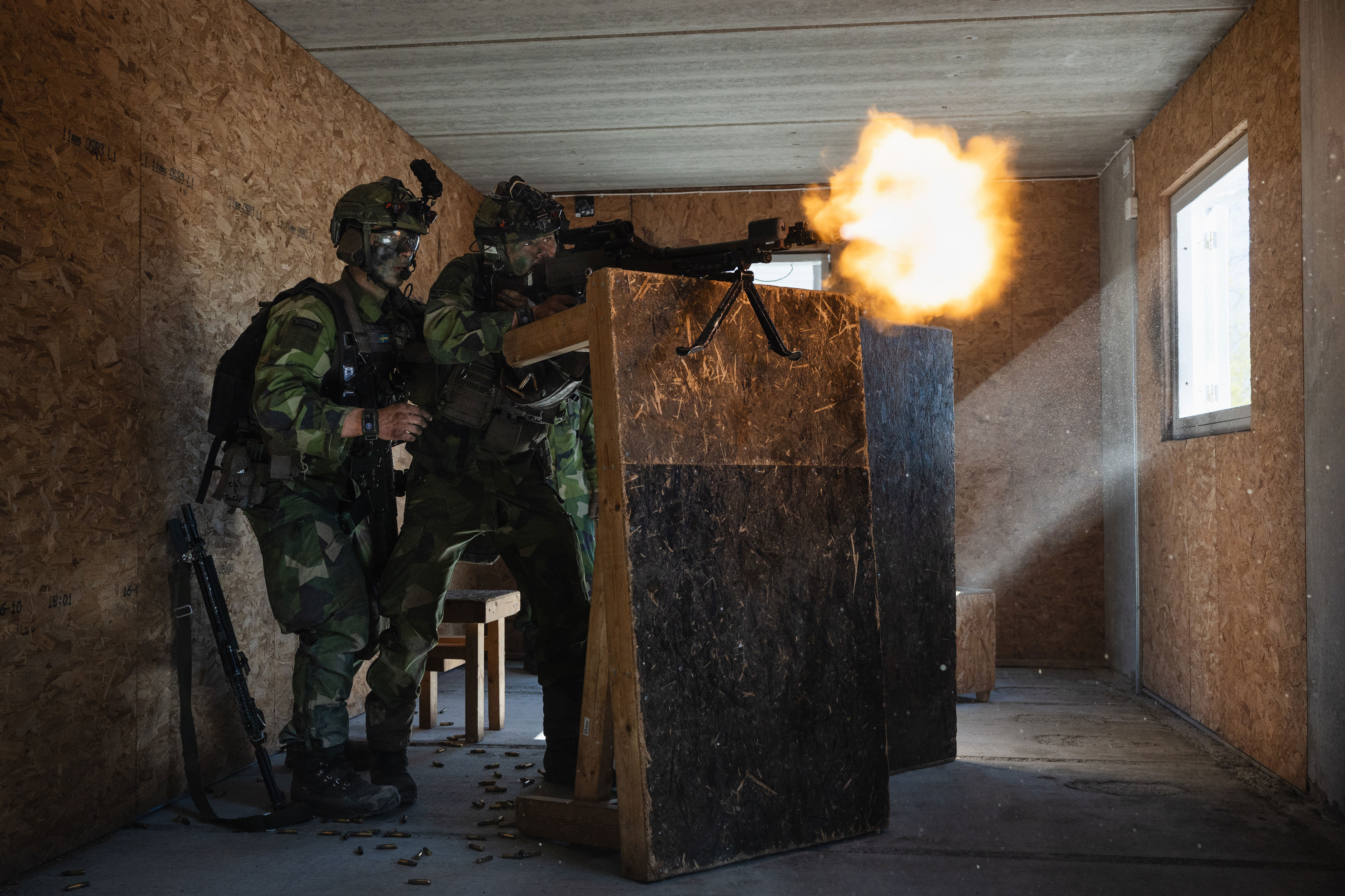 Soldater i svensk uniform avfyrar vapen med lös ammunition ut genom ett öppet fönster i en byggnad