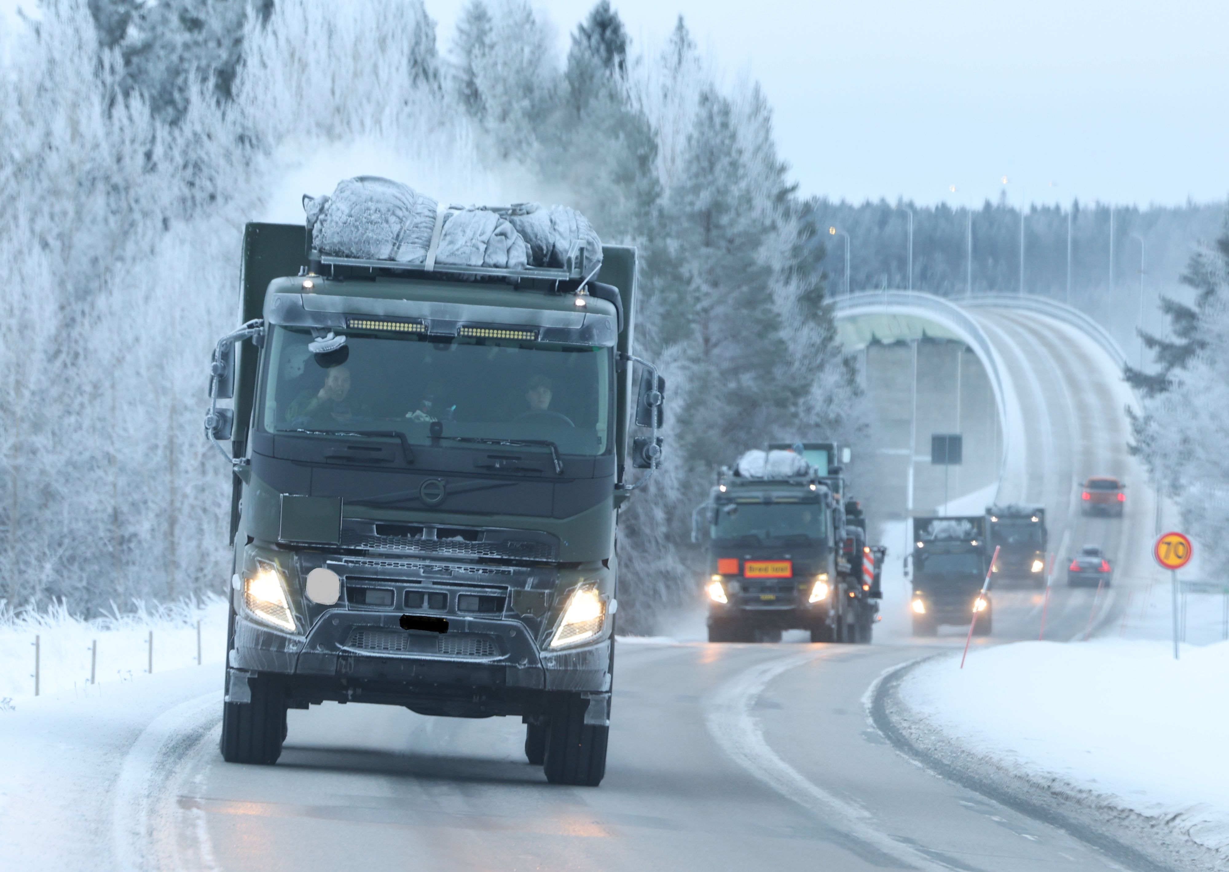 Militära lastbilar i konvoj på vinterväg.