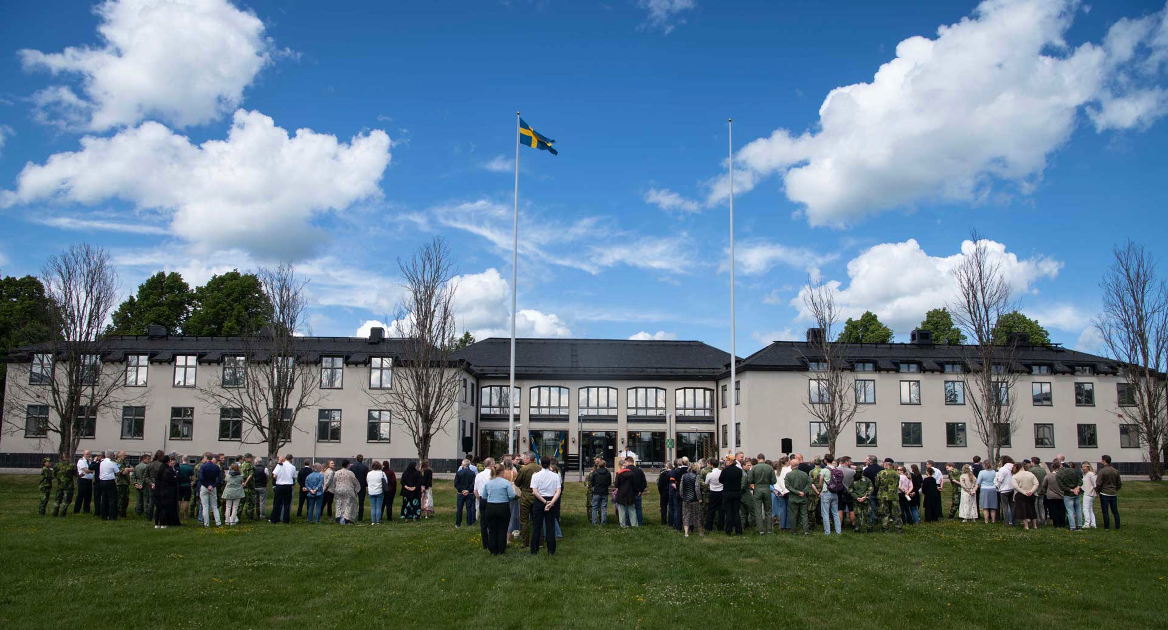 En vit bred byggnad med civila och militära personer framför