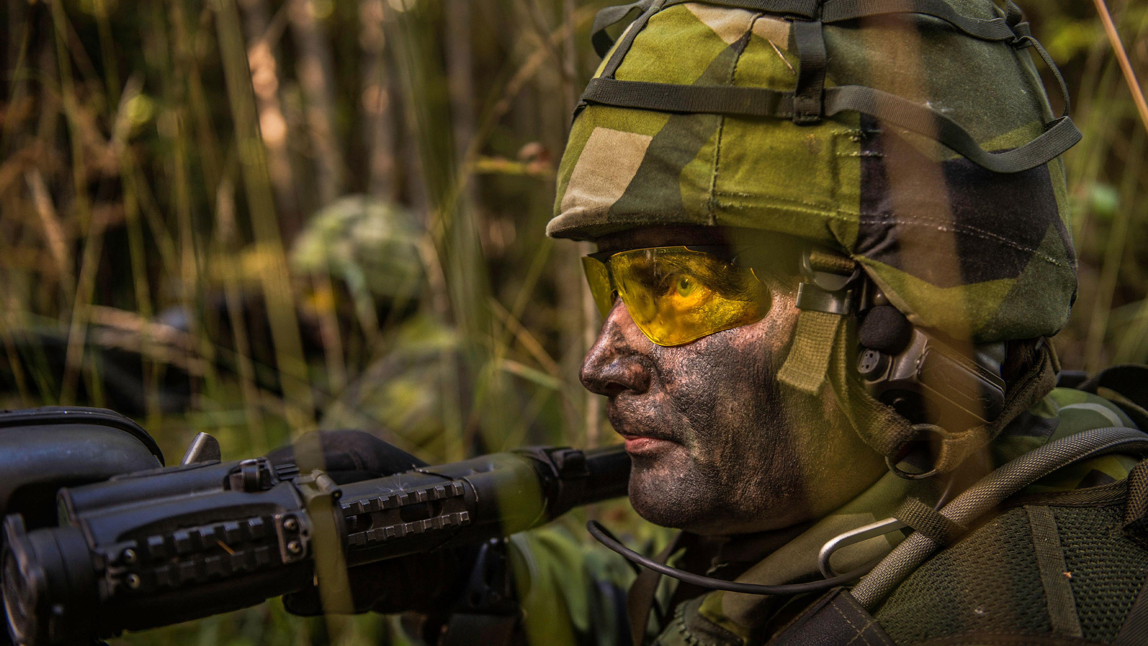 Maskerad soldat i fält siktar med sitt vapen.
