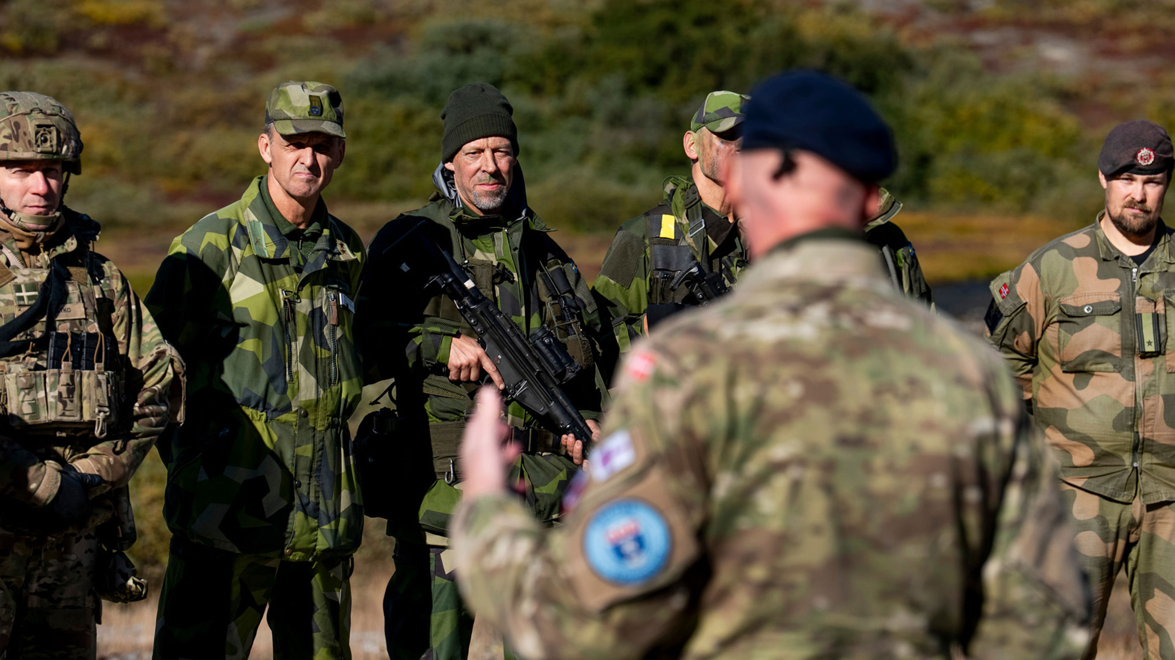 Soldater från olika länder står och lyssnar på en militär chef.