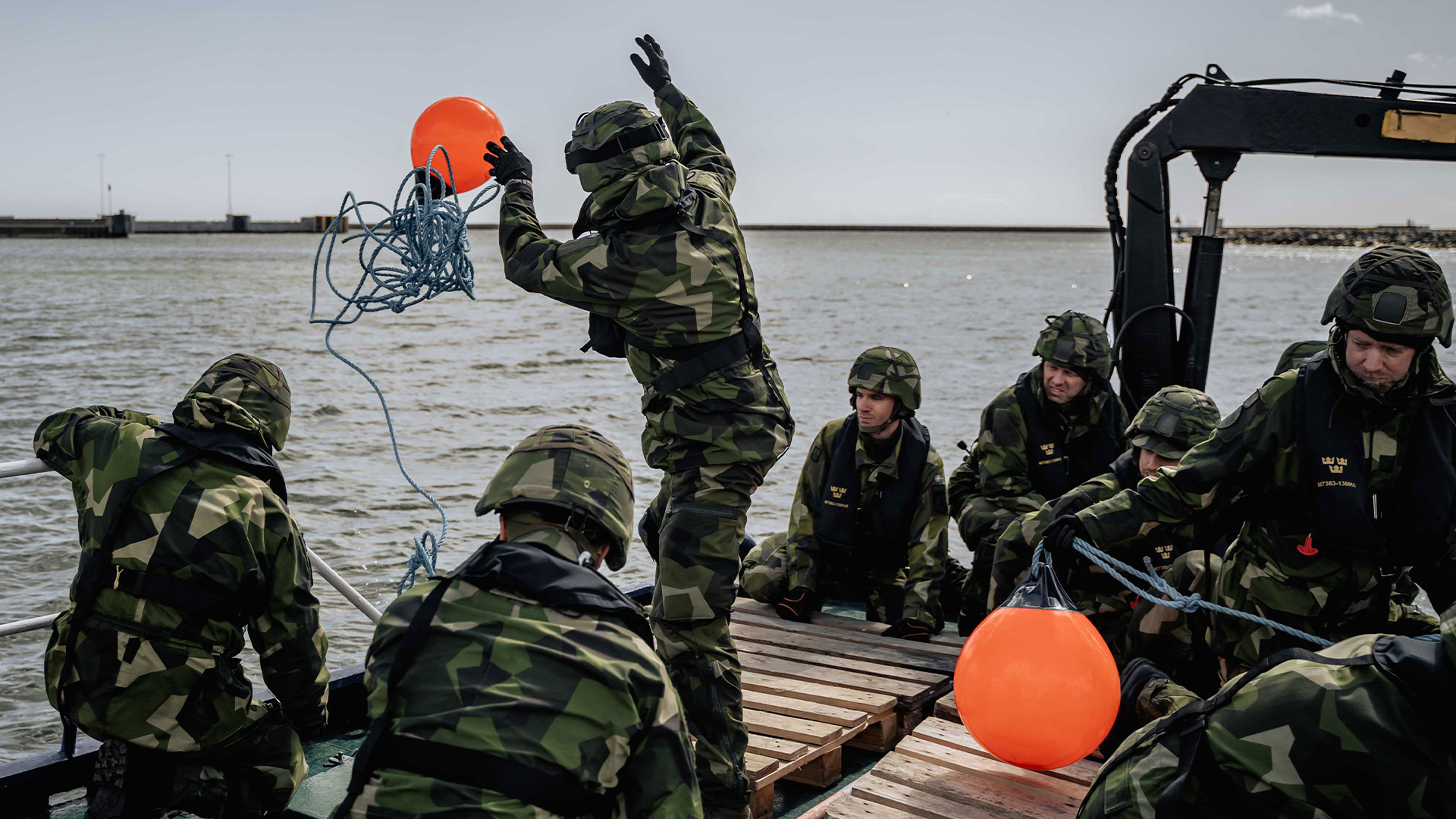 Soldater på båt. Ena soldaten slänger ut en orangea boj.