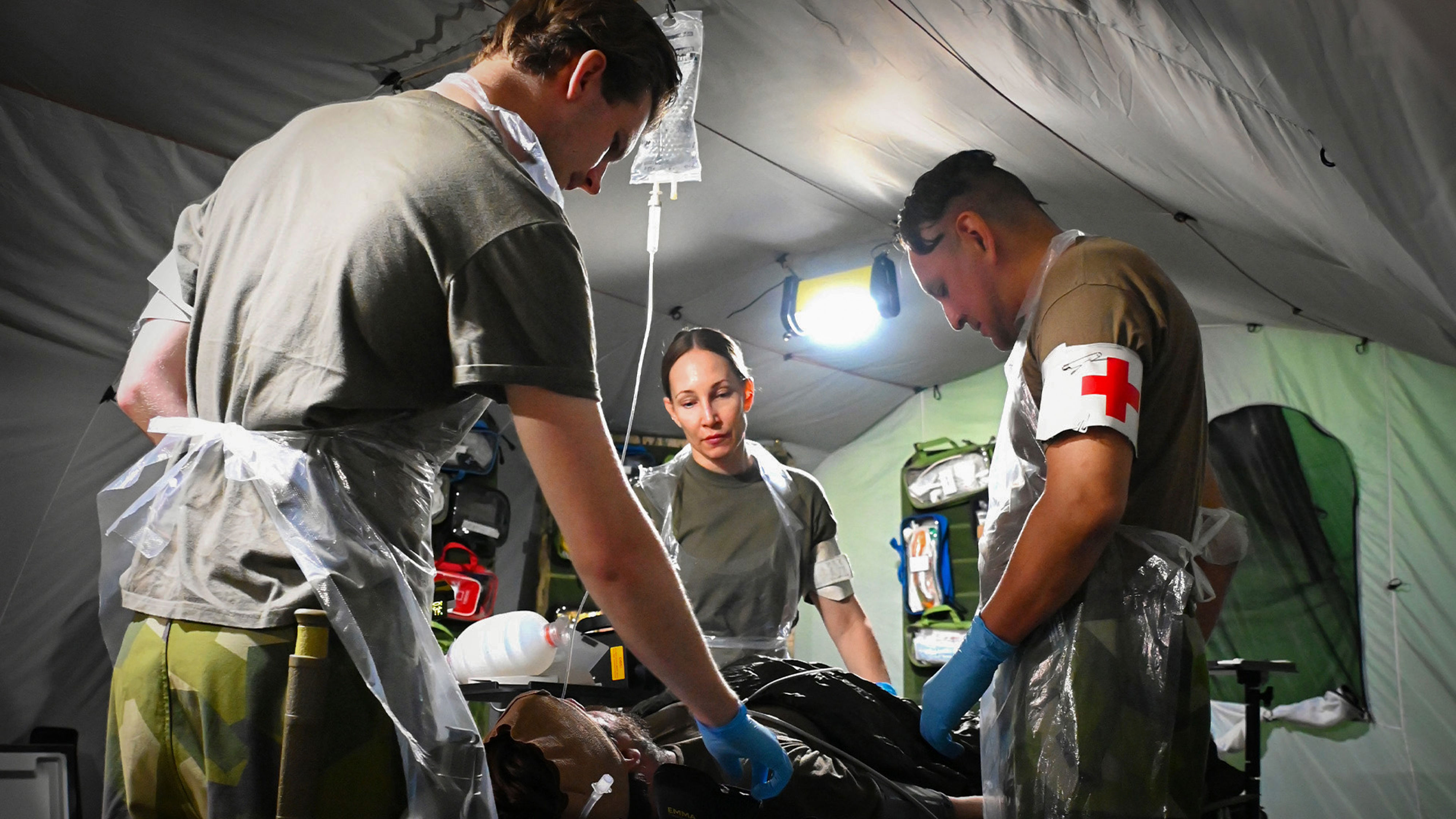 Sjukvårdare står runt ett operationsbord i militär miljö.