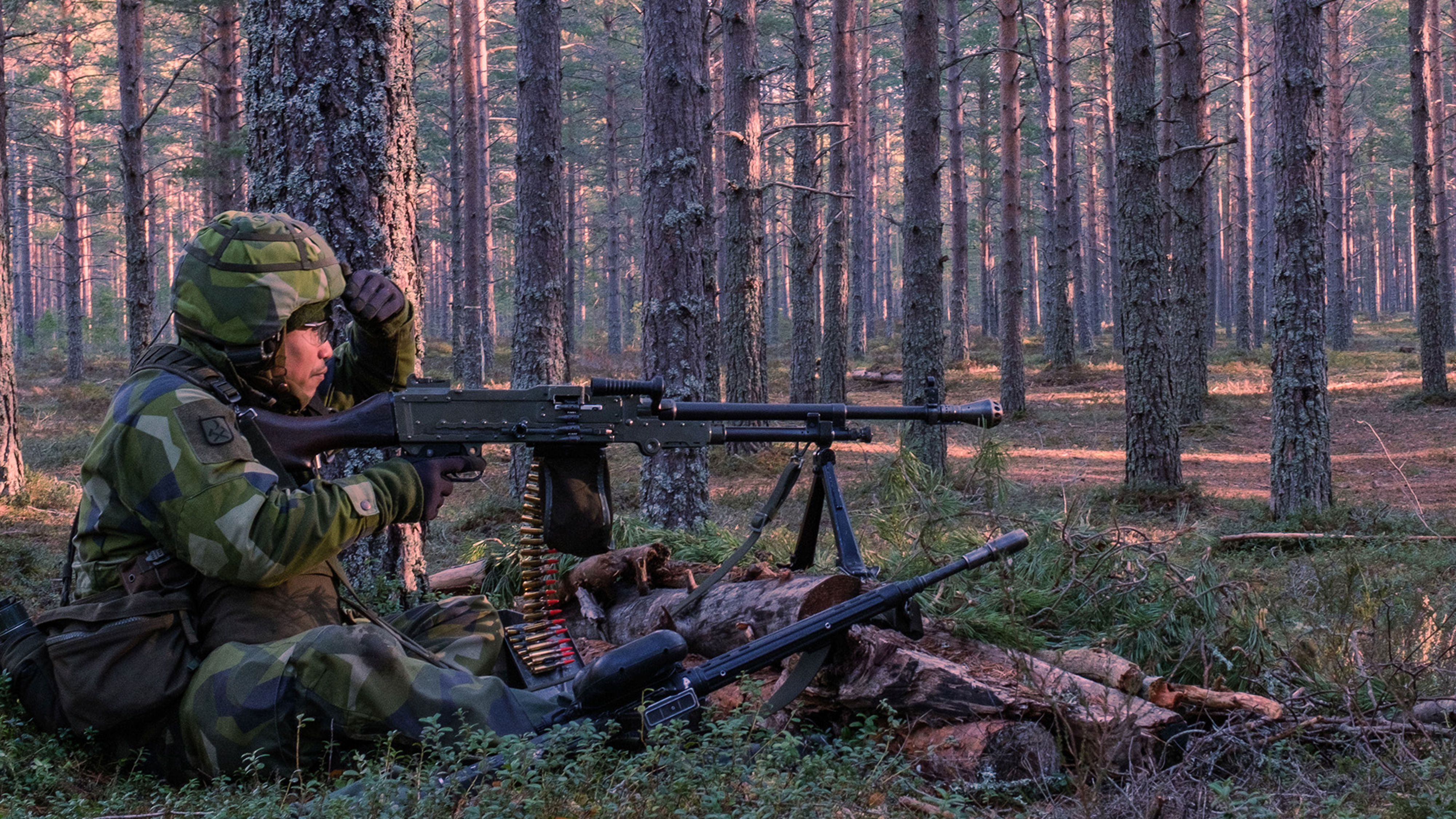 Soldat med vapen sitter i skogen och bevakar.