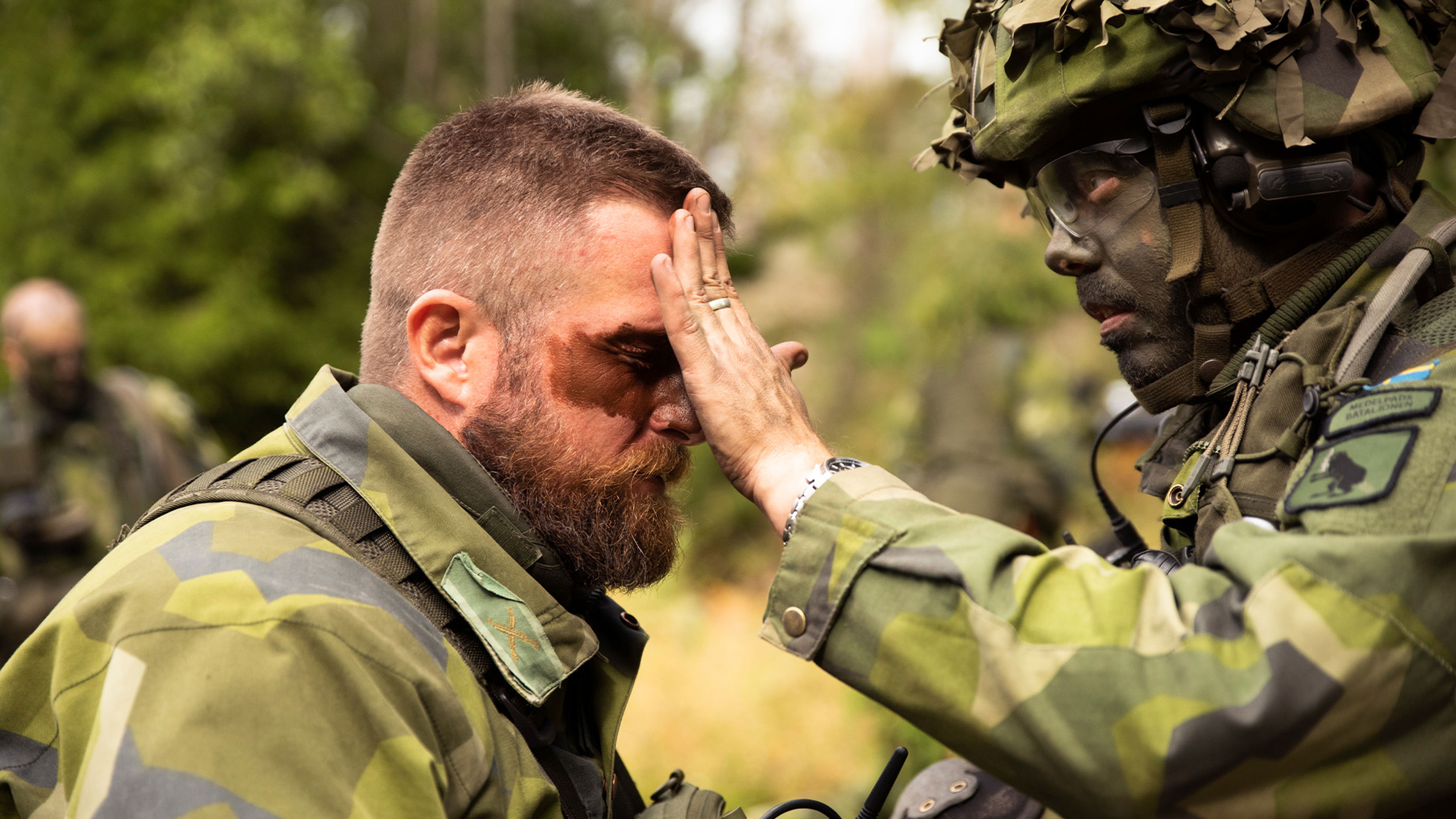 Soldat hjälper en annan soldat med maskeringsfärg i ansiktet.