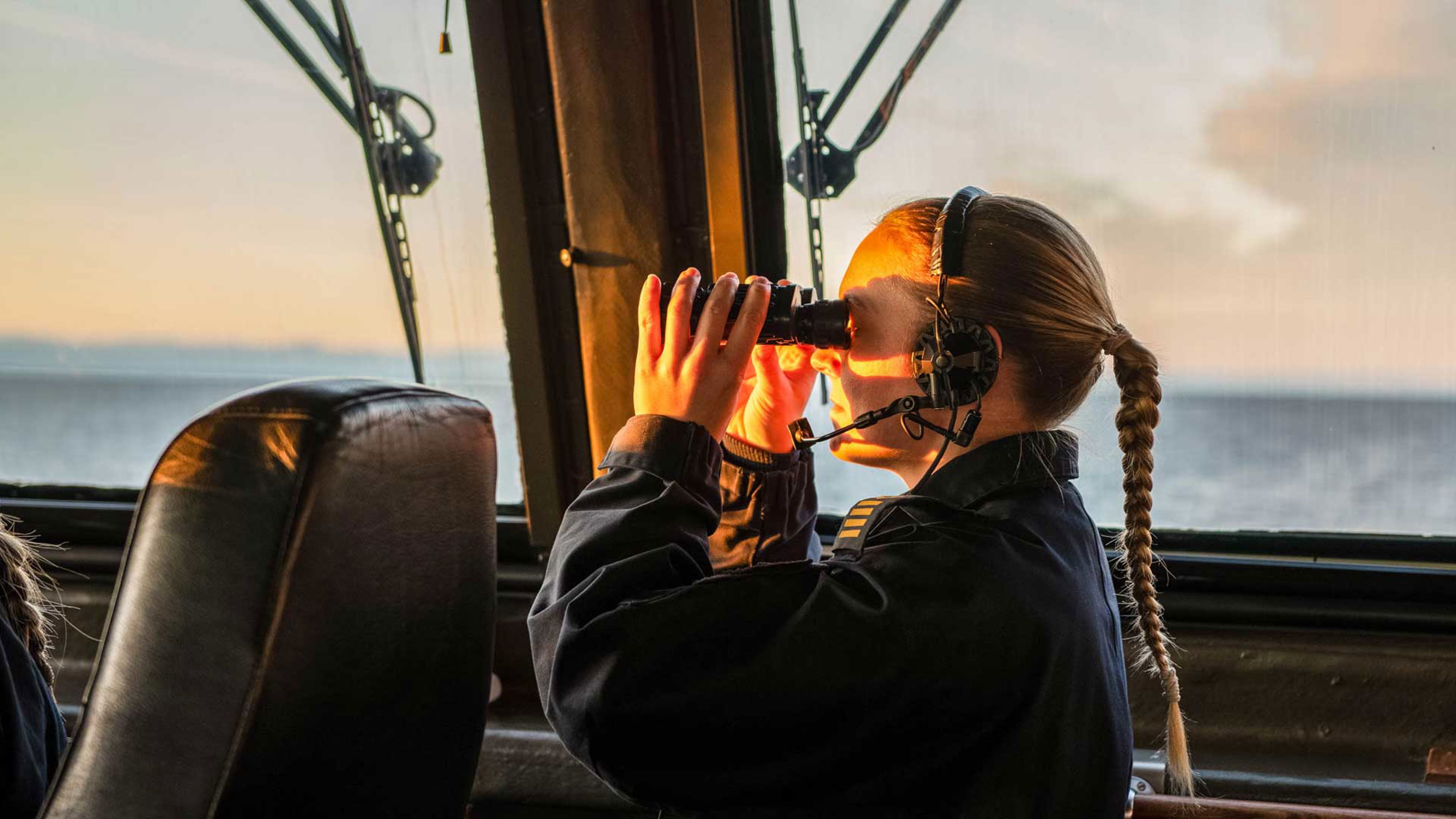 Sjöman tittar i kikare på en båt.