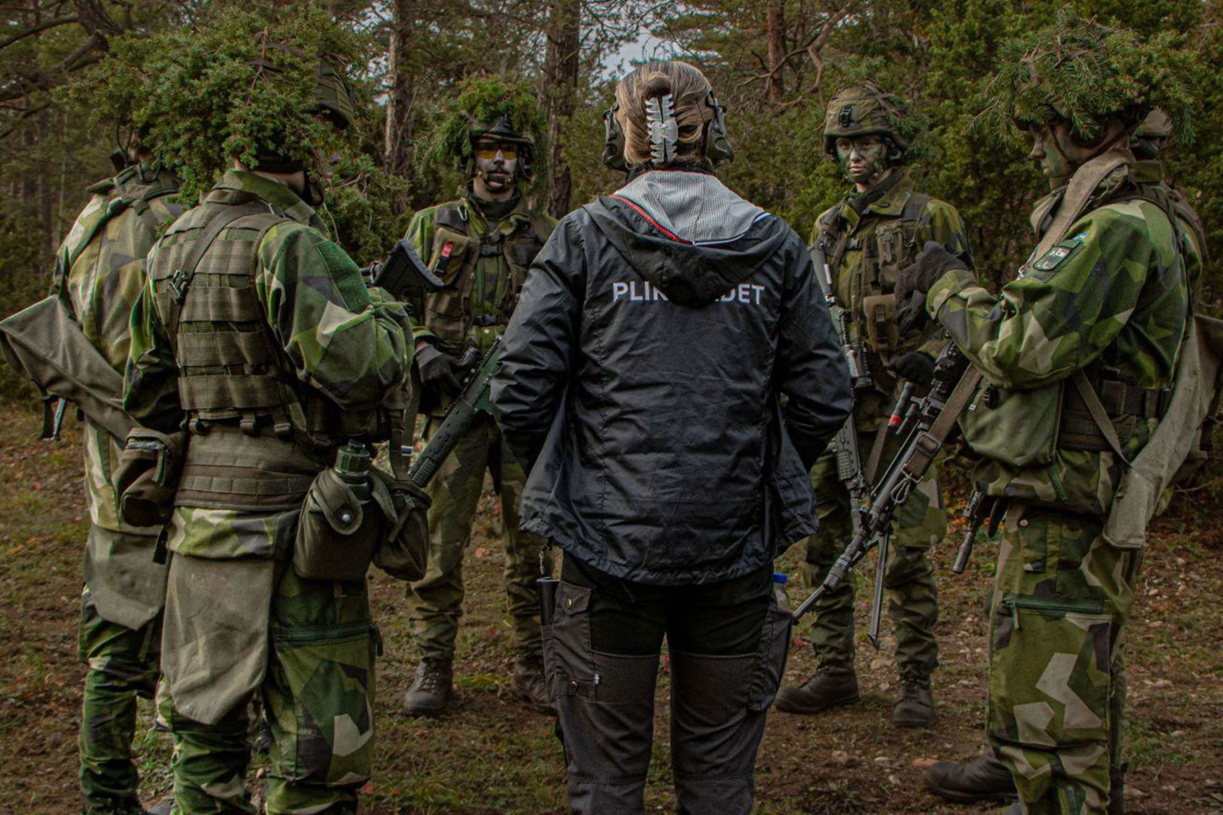 En person från Pliktrådet står tillsammans med uniformsklädda personer.