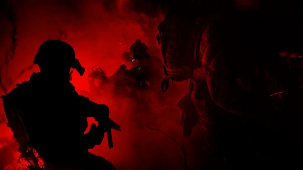 En rödsvart bild med militärer som är i ett rökmoln.