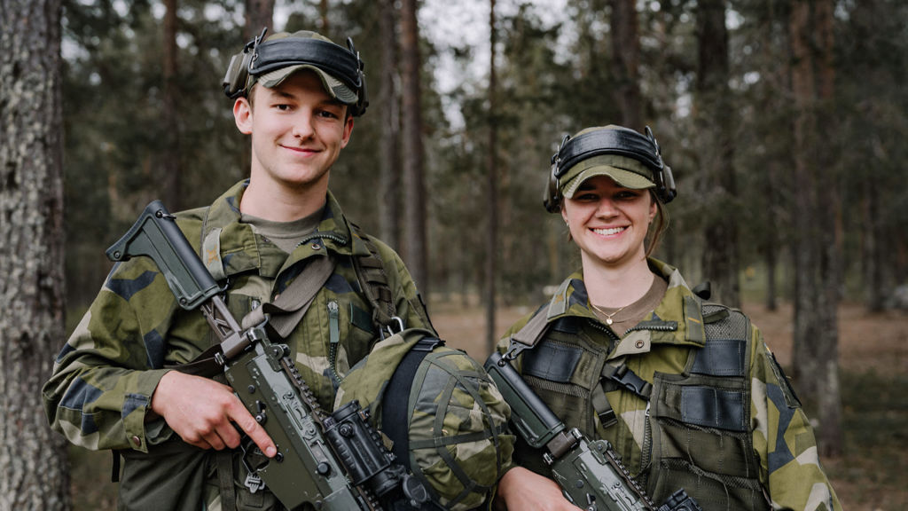 Två militärer i skogen tittar in i kameran.