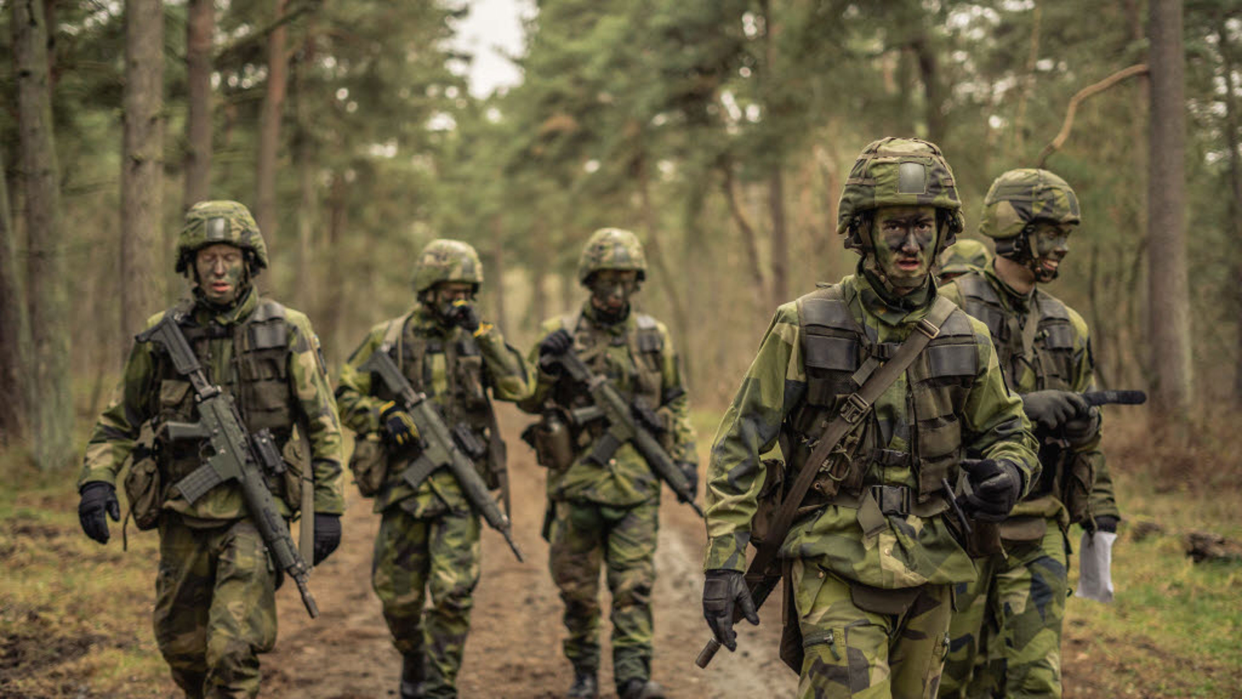 Flera militärer i full uniform går ute i fält.