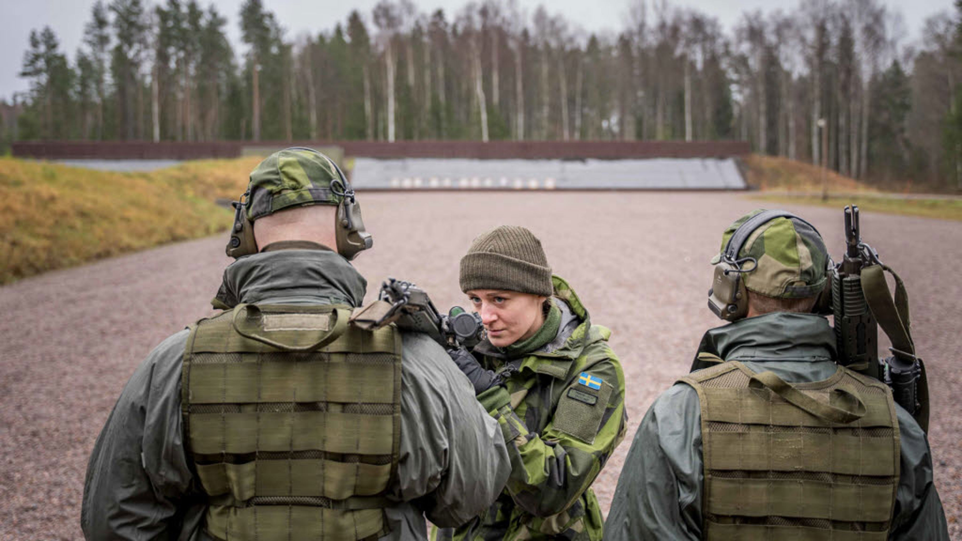 Tre uniformsklädda personer står vid ett skjutfält.