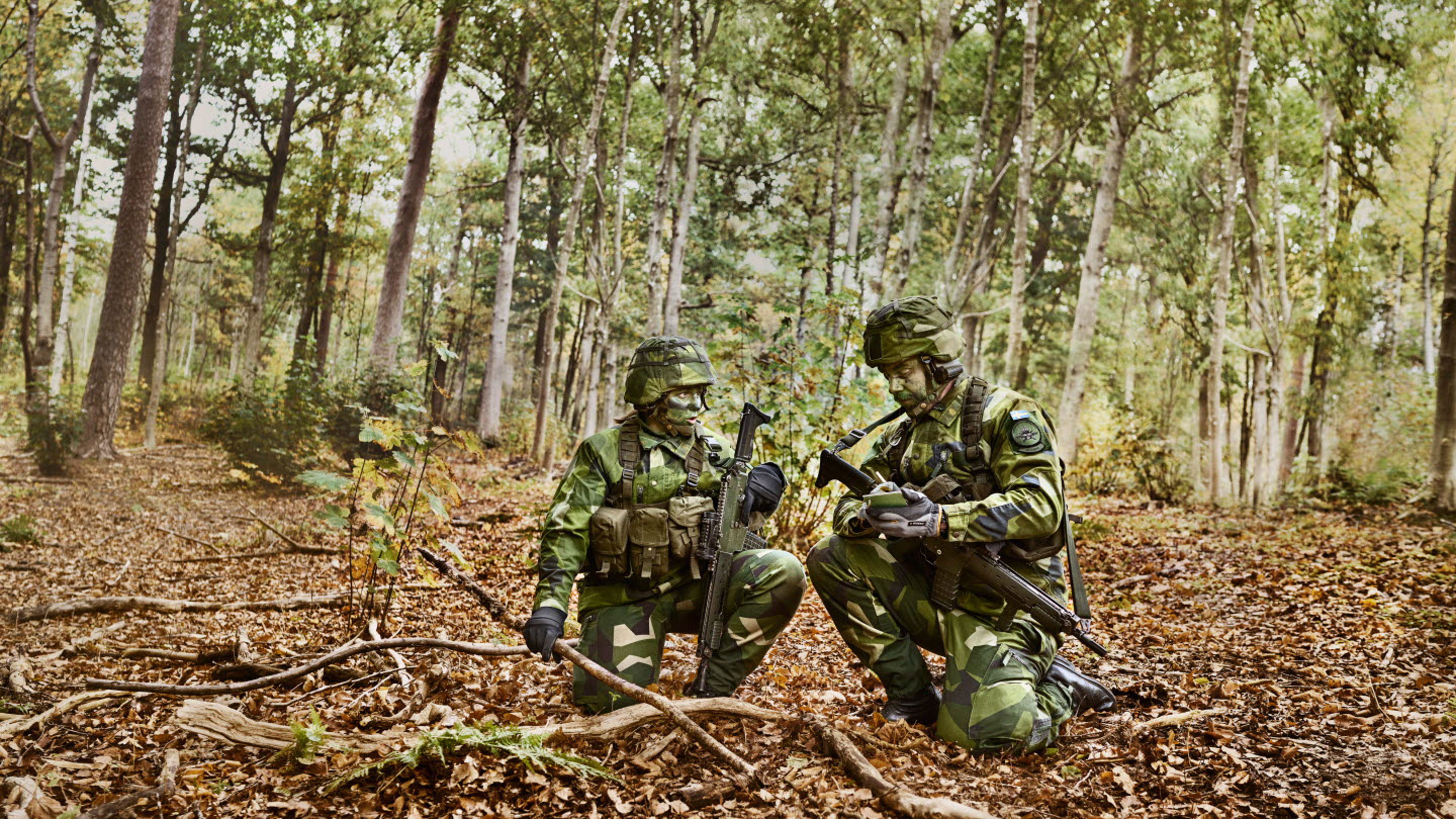 Två militärer står på huk i skogen.