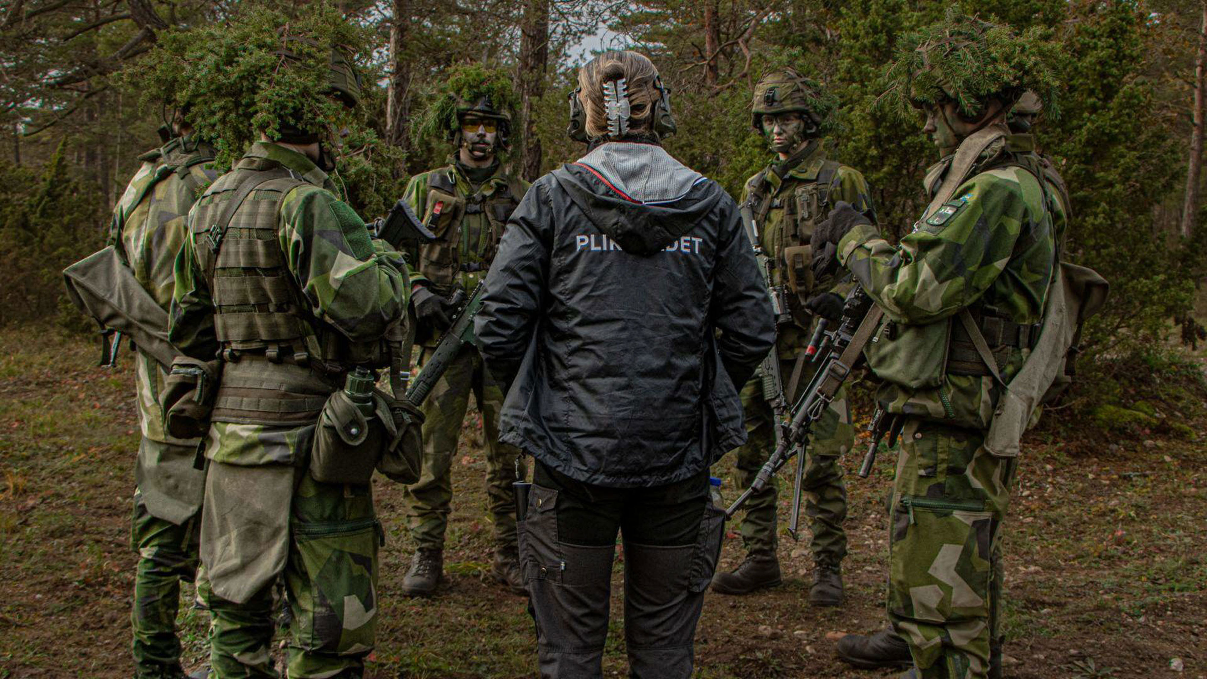 En person från Pliktrådet står tillsammans med uniformsklädda personer.